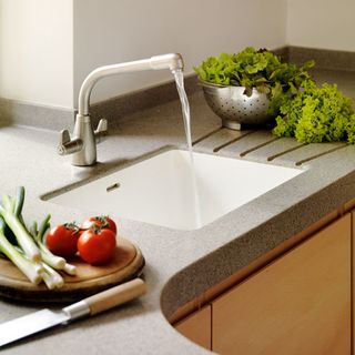 kitchen room with white sink steel tap and bowl with green vegetables