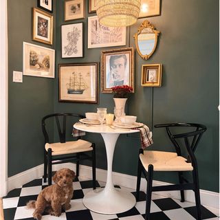 Small dining space in green painted nook with gallery wall, black and white checkered floors and pup on the floor