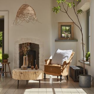 boho style living room with plant in a metal pot, beige armchair, wooden side table, wooden flooring and log burner in a fireplace