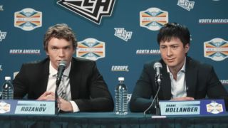 From left to right Ilya talking into a mic and Shane looking forward during a press confrence in Heated Rivalry.