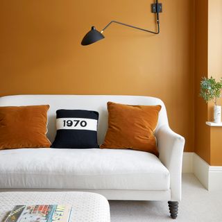 Living room with ochre walls, white sofa and black wall light