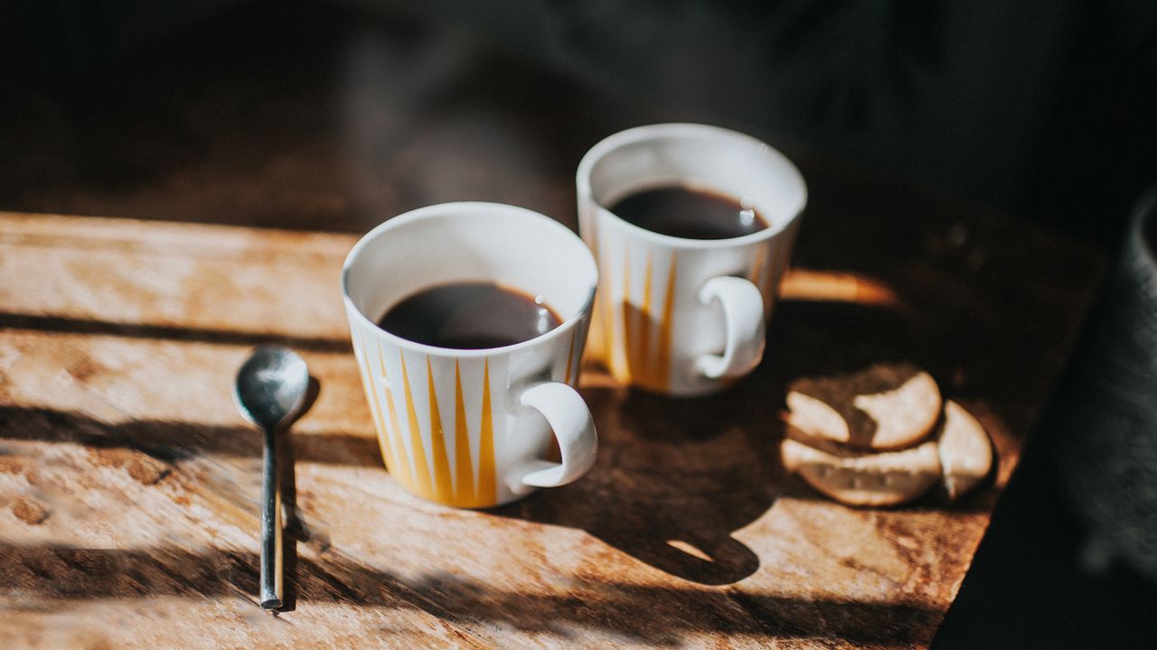 Two mugs of warm coffee on a sunlit table