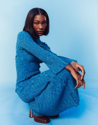 Demi Singleton poses in front of blue backdrop wearing a long sleeve knit dress.