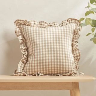 A pale green gingham cushion on a pale bench in front of a cream background