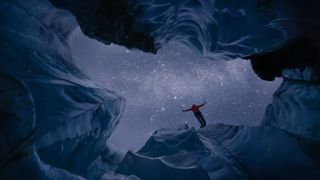 From the interior of a glacier, a person standing on the edge and the night sky are visible.
