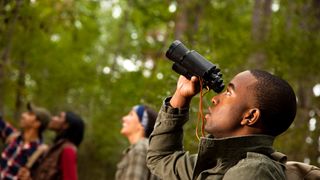 Man using binoculars whilst hiking in the woods with his friends
