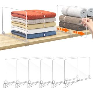 Clear plastic slide-on shelf dividers on a wooden shelf with piles of folded clothing on them. 