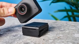 a black small 4K webcam with a red button photographed on a beige surface against a blue background