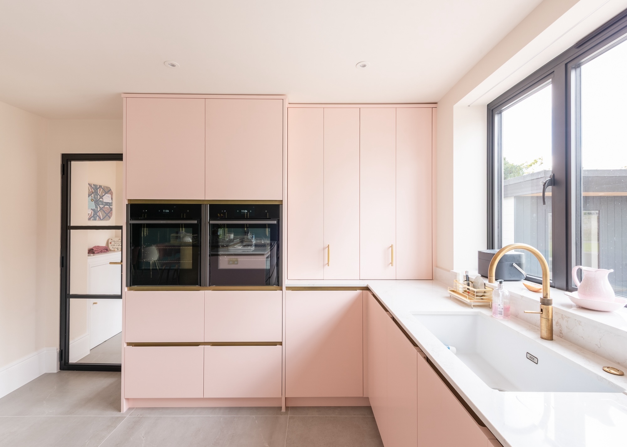 a blush pink kitchen with a mix of gold hardware, white worktops and pale wood flooring