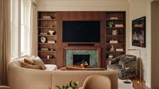 Living room with warm white walls, dark wood media wall joinery, curved beige sofa and Dedar patterned grey and white armchair