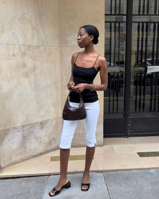 Sylvie Mus wearing a black camisole with white capri pants, a brown bag, and black block heel sandals.