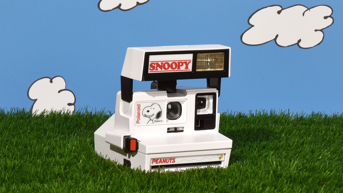 Retrospekt Snoopy Polaroid instant camera on grass with cartoon clouds on blue sky background