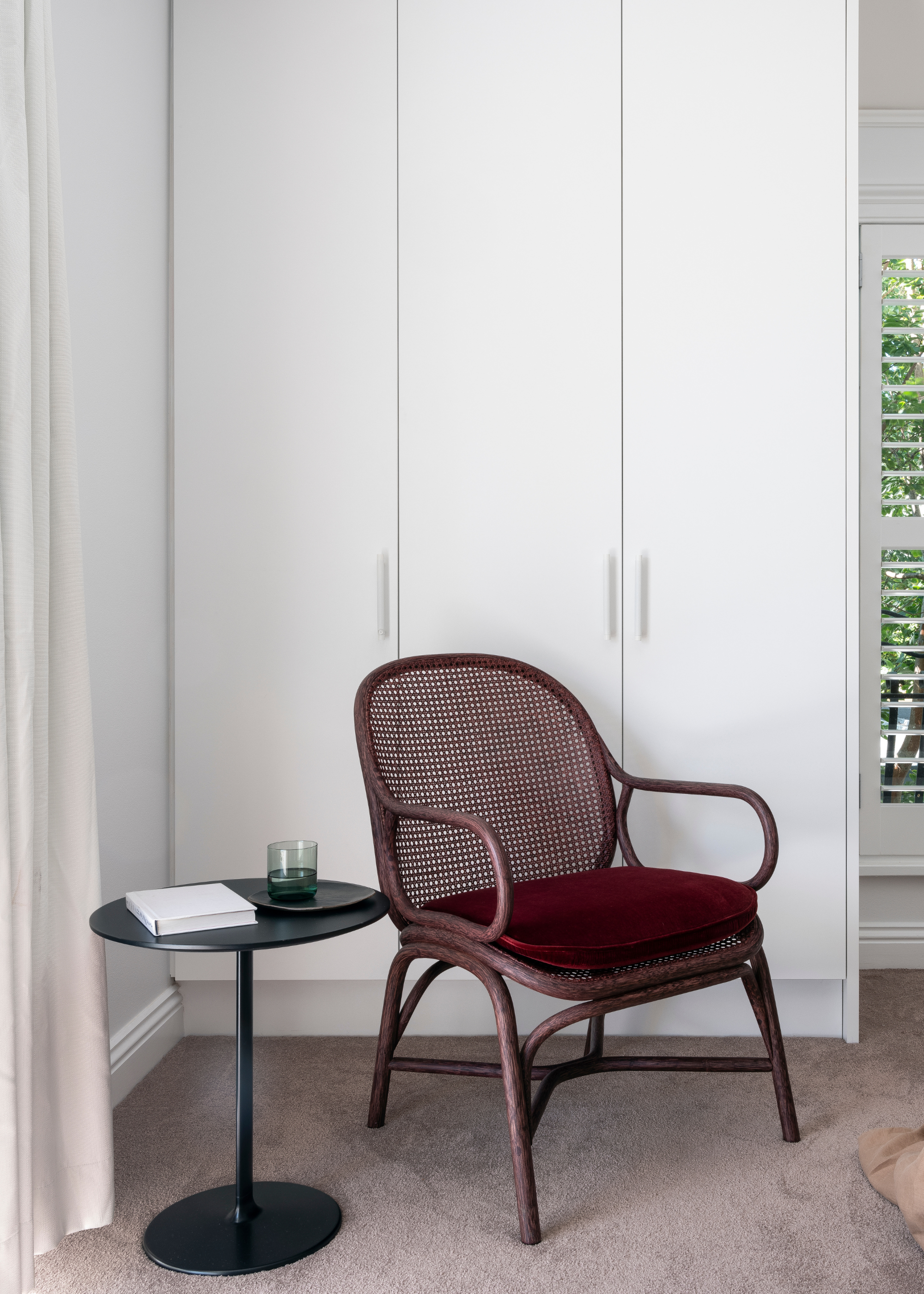 A white closet, a maroon chair and a black side table