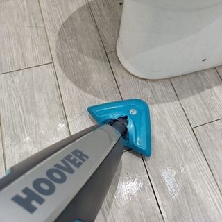 First person view of a Hoover steam cleaner being used on a tile floor around the base of a toilet.