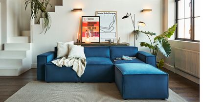 A low-level L-shaped teal velvet sofa in a living room with two sconces as living room wall lighting ideas