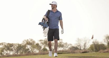 A man with Academy Sports golf gear walks through a golf course