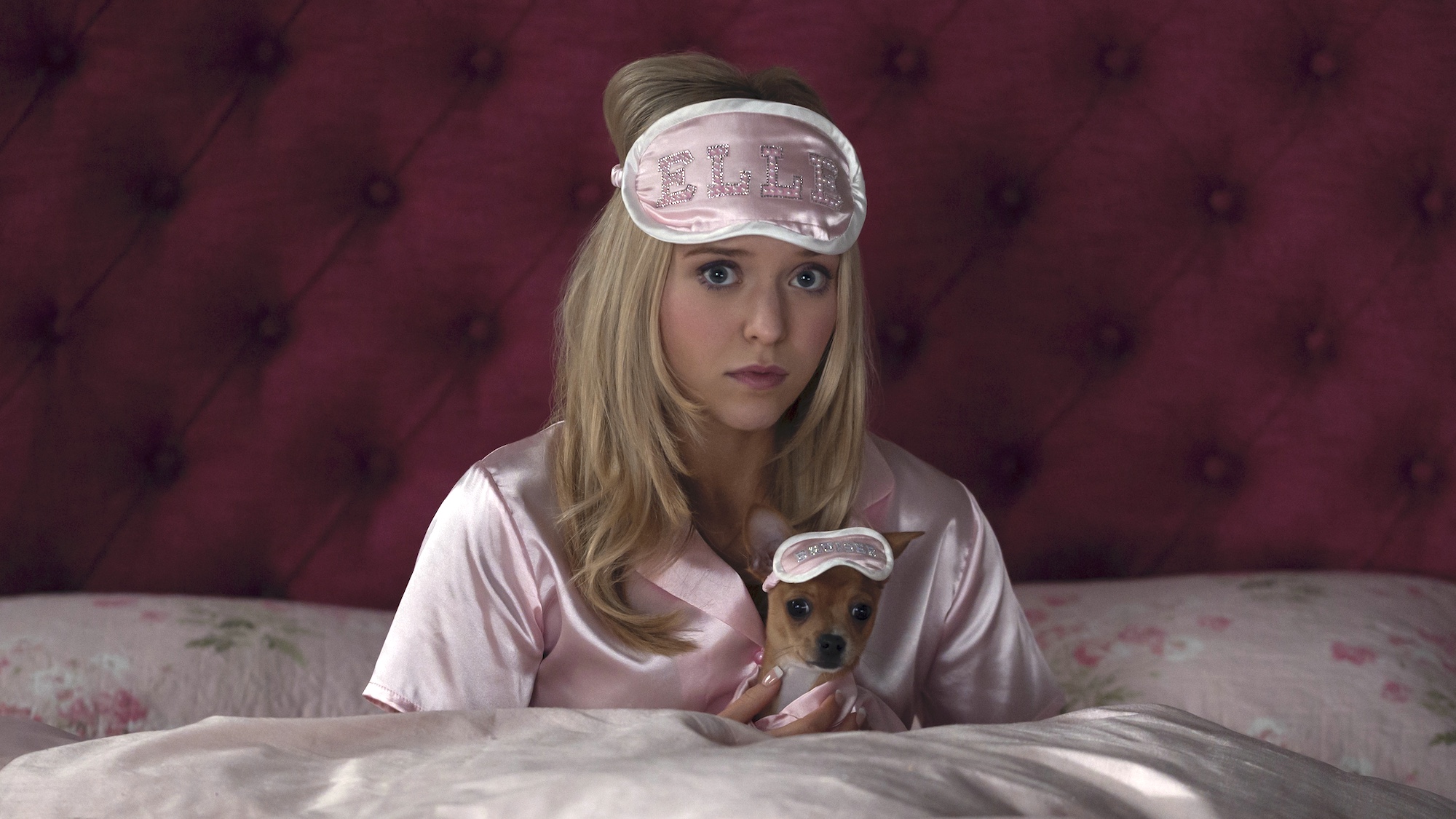 Lexi Minetree as Elle Woods in matching light pink pajamas with Bruiser sitting up in bed in Elle series 