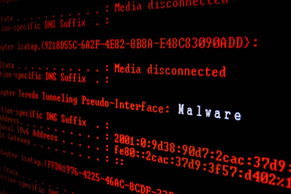 A close up image of red computer code on a black screen with the word malware displayed in white