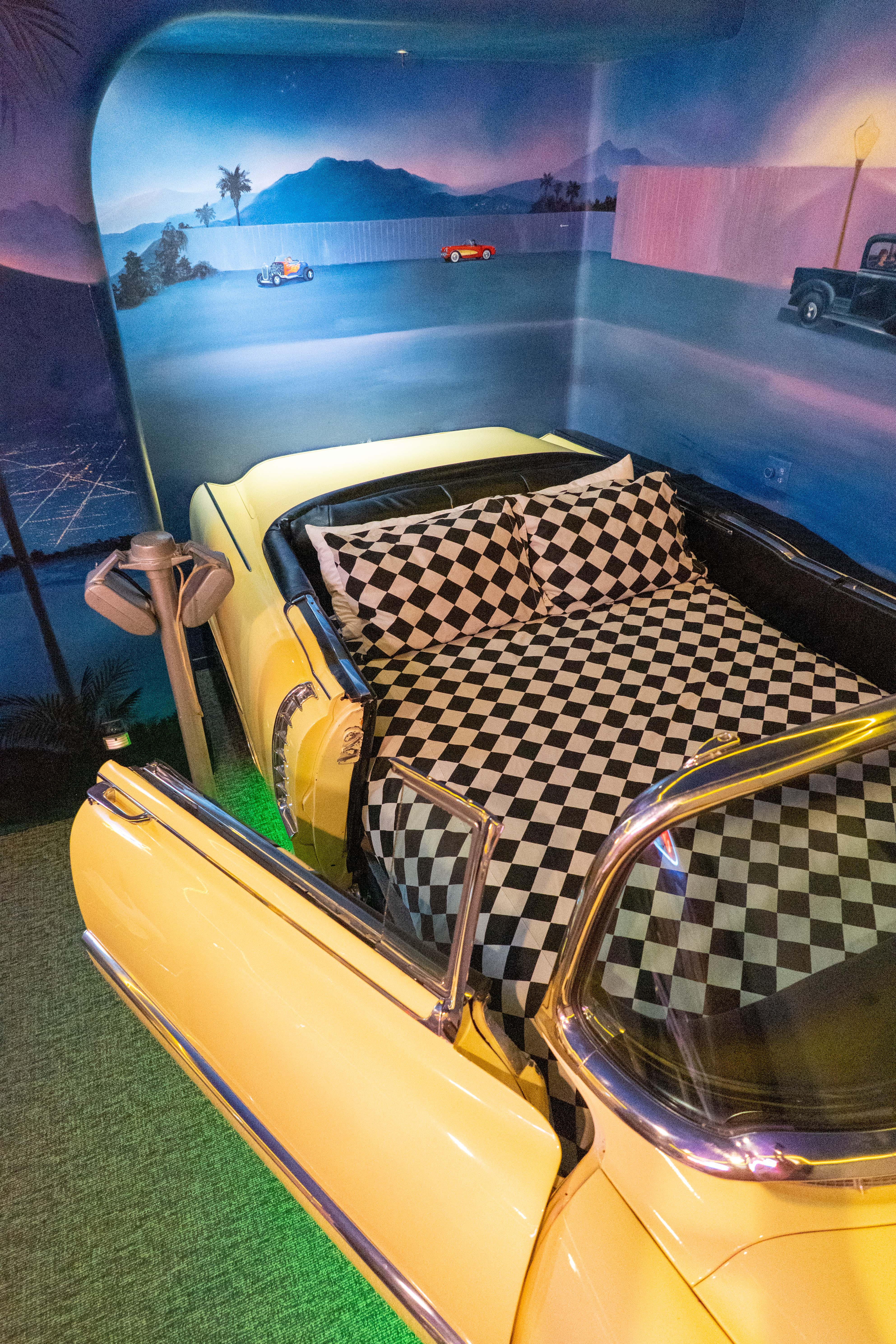 A yellow Cadillac converted into a chequered black and white bed sits in a whimsically decorated room inspired by the 1950s.