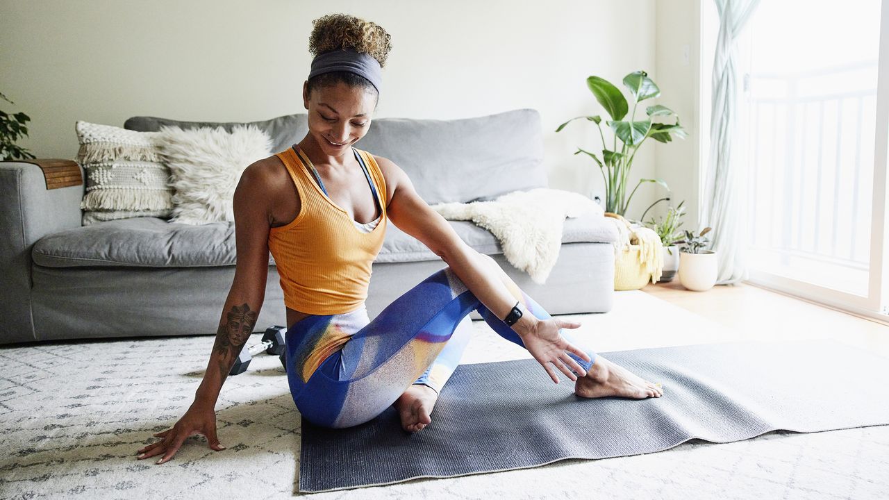 Woman practicing yoga at home, barefoot on a mat, performing a seated pose