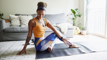 Woman practicing yoga at home, barefoot on a mat, performing a seated pose