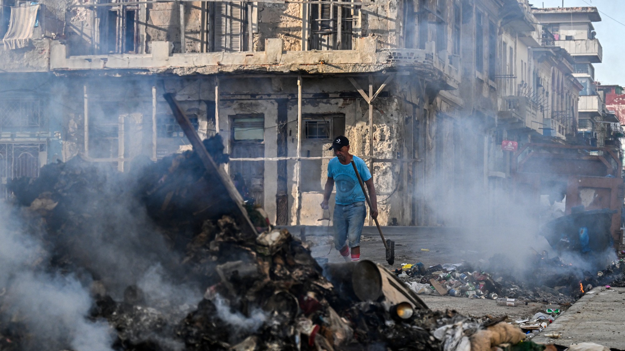 A man walking the streets of Cuba, with piles of rubbish set on fire