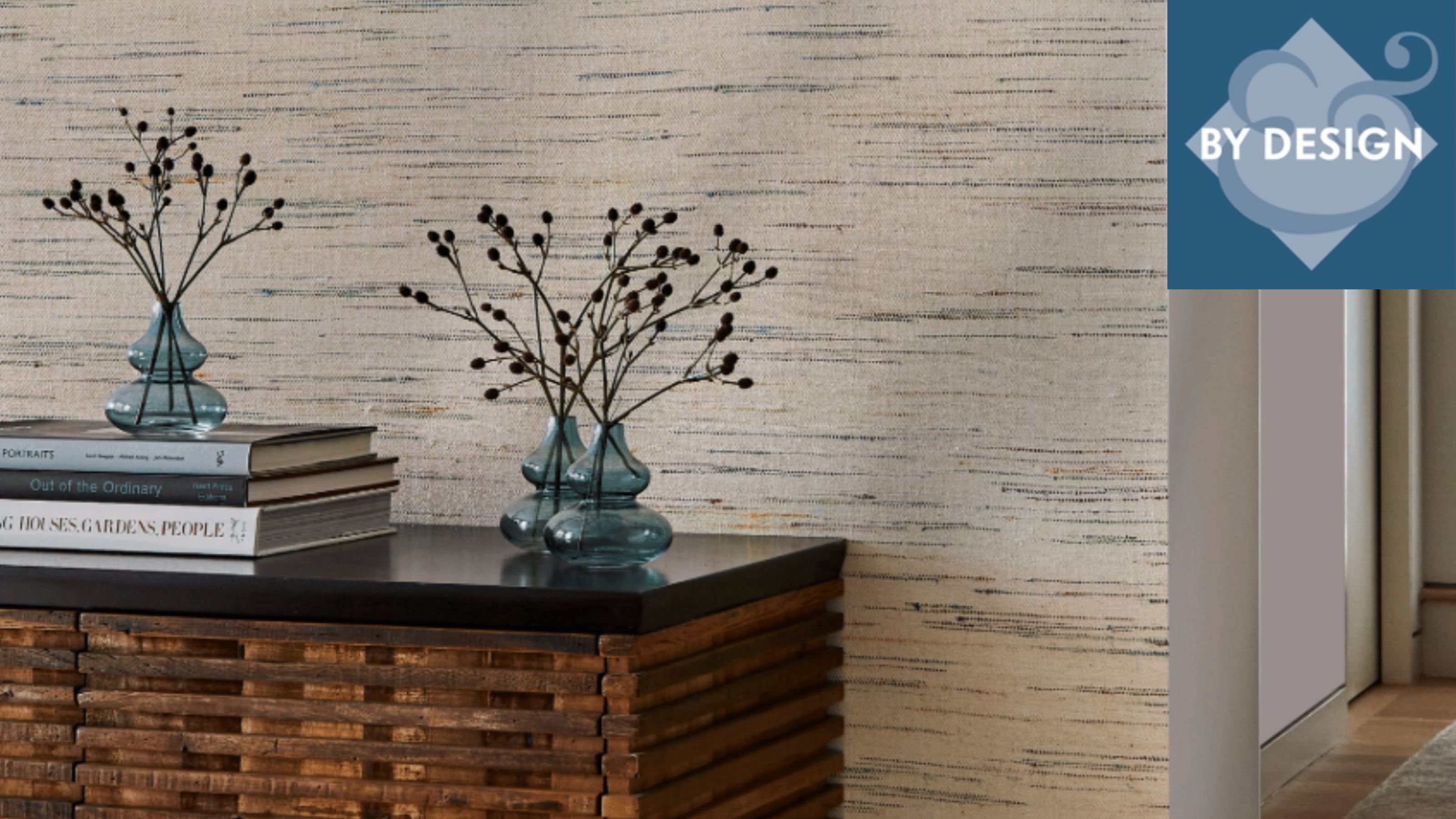 Close up of wooden console table decorated with vases and books, textured wallcovering behind, corridoor with wooden flooring to the right