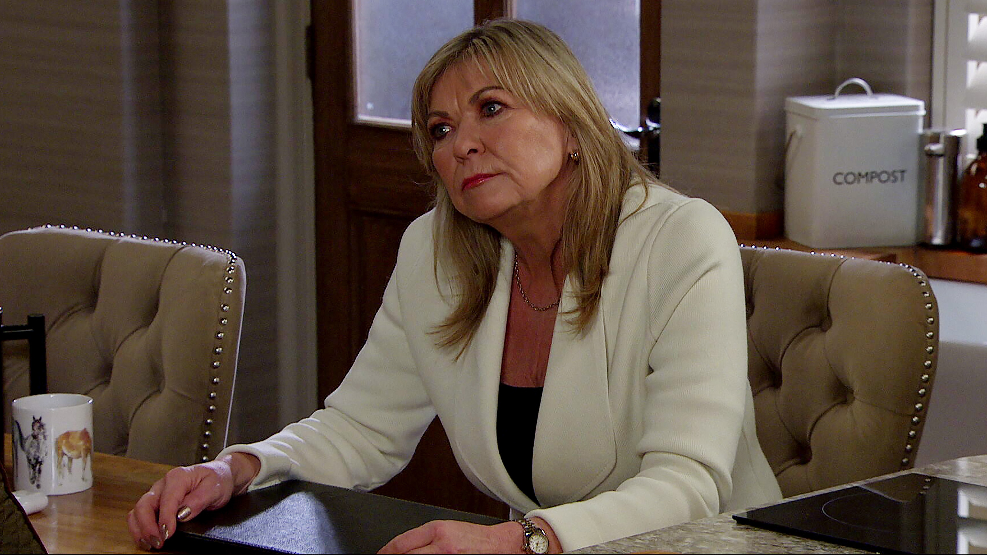 Kim Tate looks at something off screen wearing a white blazer.