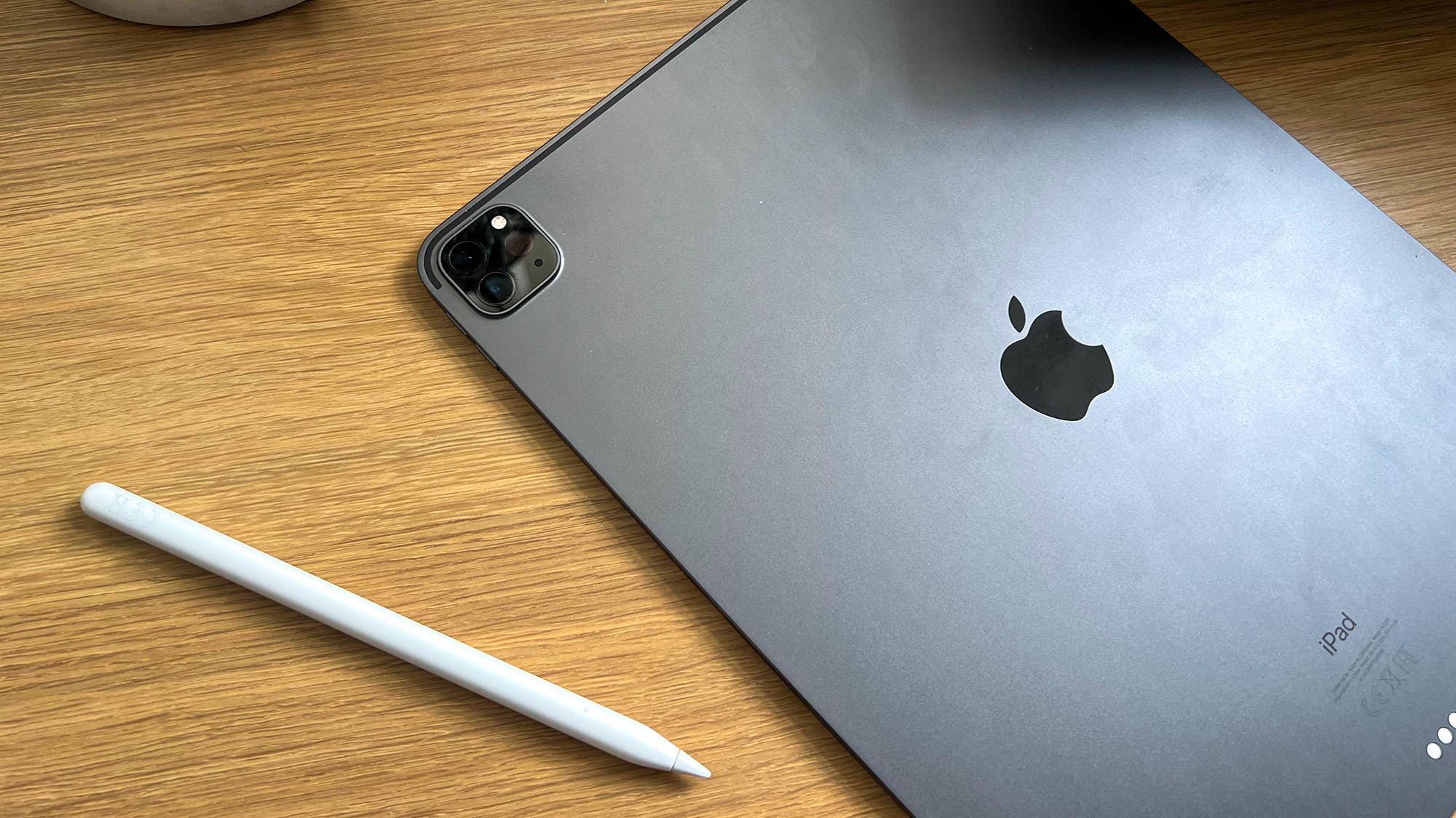 A photograph of the Apple Pencil on a table next to the 12.9in Apple iPad Pro