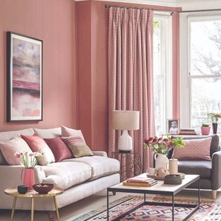 A living room with a wall covered in a dusty pink wallpaper with coordinating curtains on the window