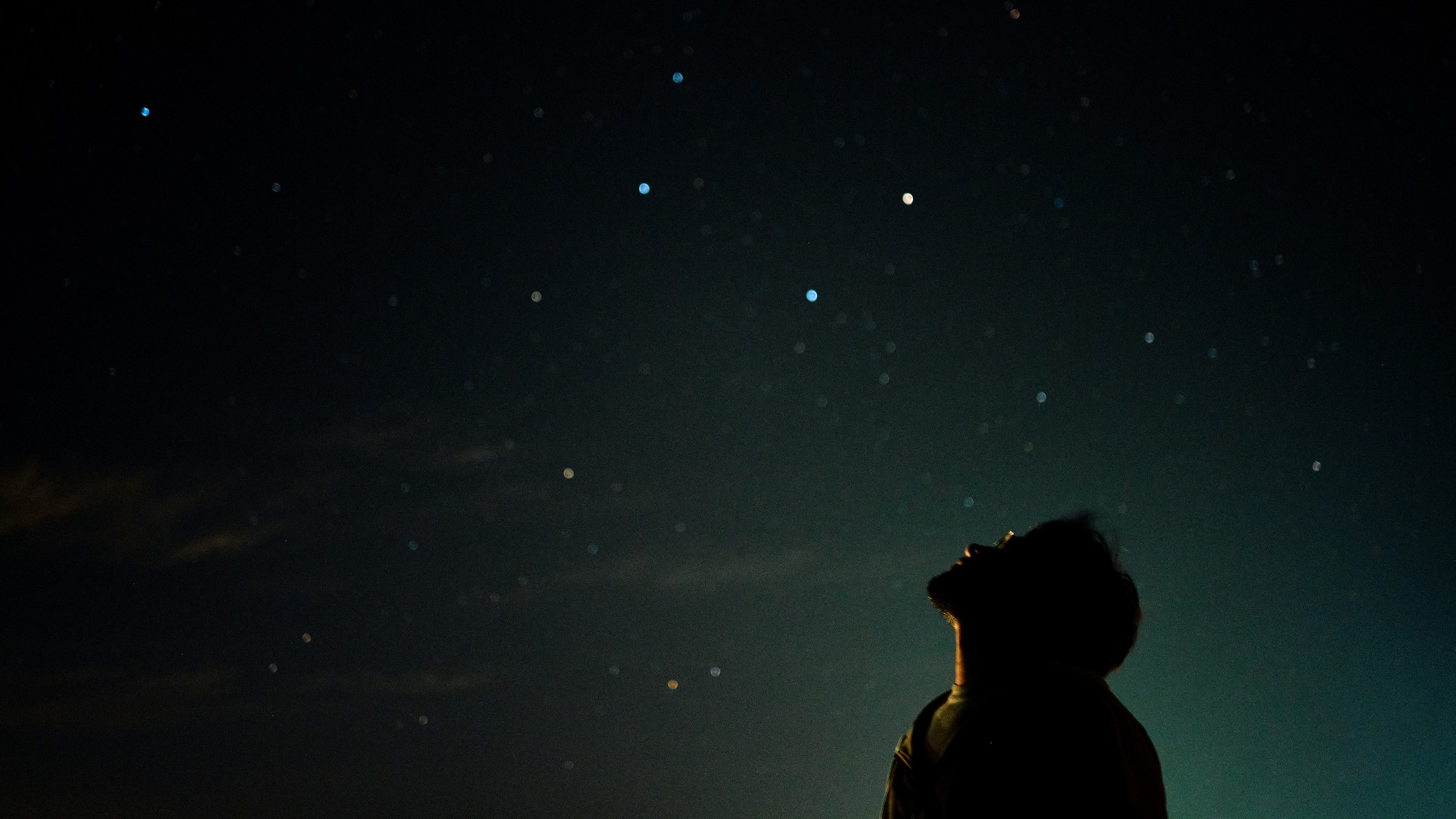 a man looks up at the night sky above.