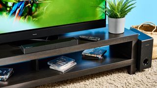 the ultimea nova s50 a black compact soundbar with LED on the front and a wired subwoofer is photographed on a black TV mount connected to a panasonic TV 