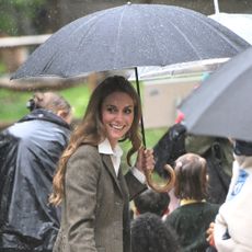 Kate Middleton holding a black umbrella in the rain surrounded by people
