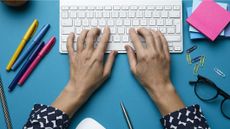 The best keyboard hero image showing a keyboard on a desk covered with stationary being typed upon