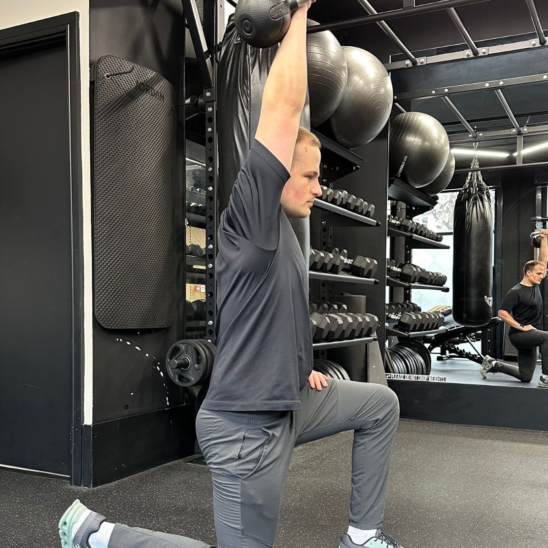 Personal trainer Ollie Thompson demonstrating a helf-kneeling shoulder press