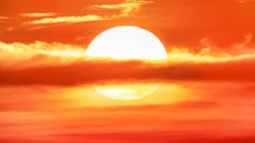 A cloud bisects the sun setting in an amber sky.