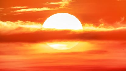 A cloud bisects the sun setting in an amber sky.