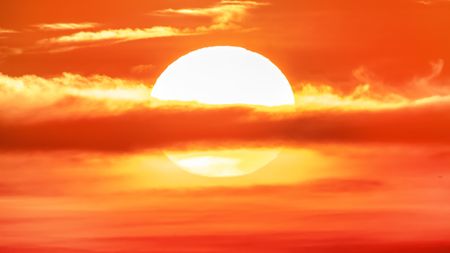 A cloud bisects the sun setting in an amber sky.