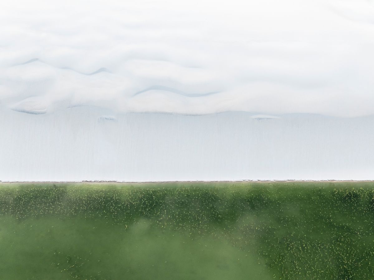 Aerial view of soft clouds above a vast green field, creating a serene yet striking contrast between sky and land