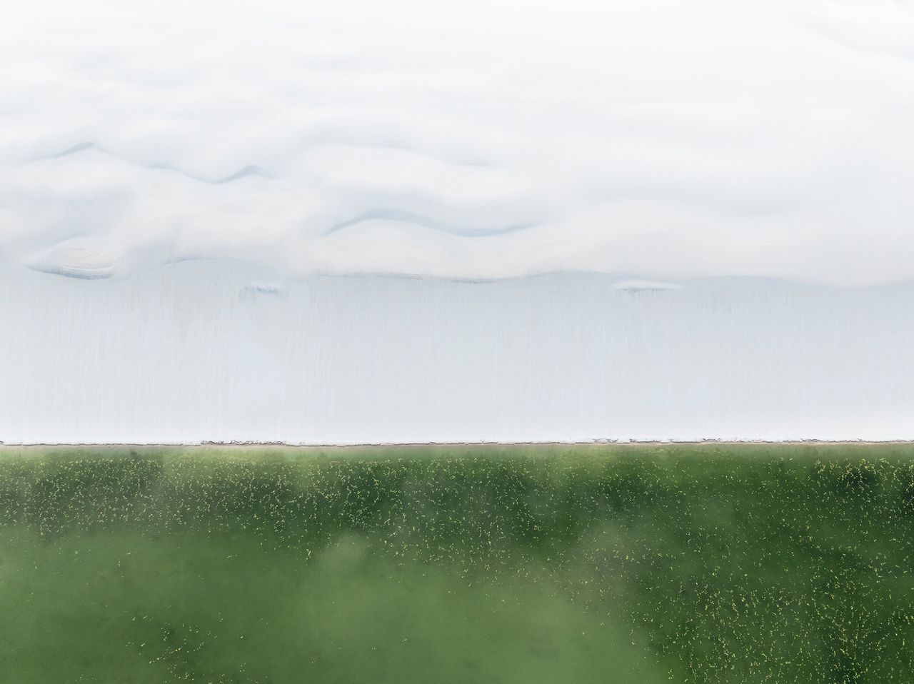 Aerial view of soft clouds above a vast green field, creating a serene yet striking contrast between sky and land
