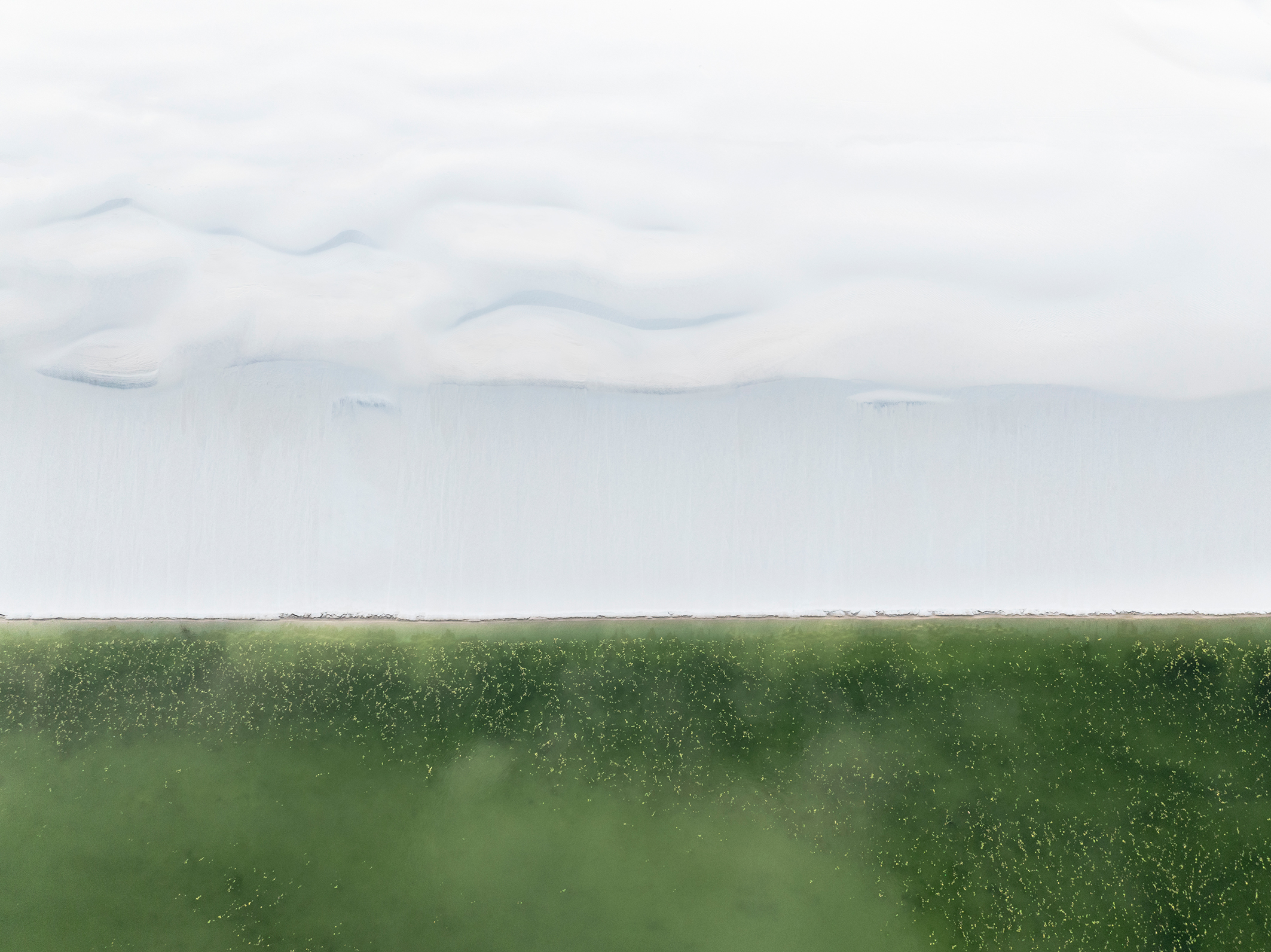 Aerial view of soft clouds above a vast green field, creating a serene yet striking contrast between sky and land