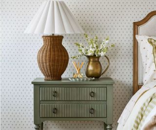 Wooden bedside table in sage green with rattan lamp, gold vase and diffuser