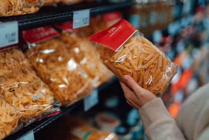 Person holding a pack of pasta in a supermarket aisle
