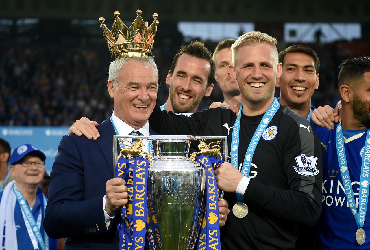 LEICESTER, ENGLAND - MAY 07:Claudio Ranieri poses with the Premier League Trophy while Kasper Schmeichel puts the crown on the head of the manager as players and staffs celebrate the season c