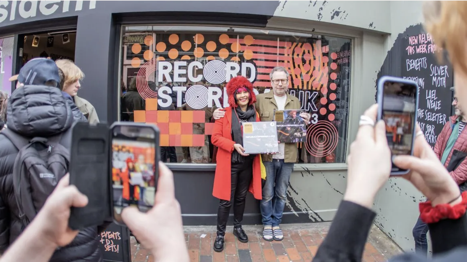 شخصان يقفان أمام متجر الفينيل لتصويرهما. تعرض النافذة ملصقات يوم مخزن السجلات الرسمية