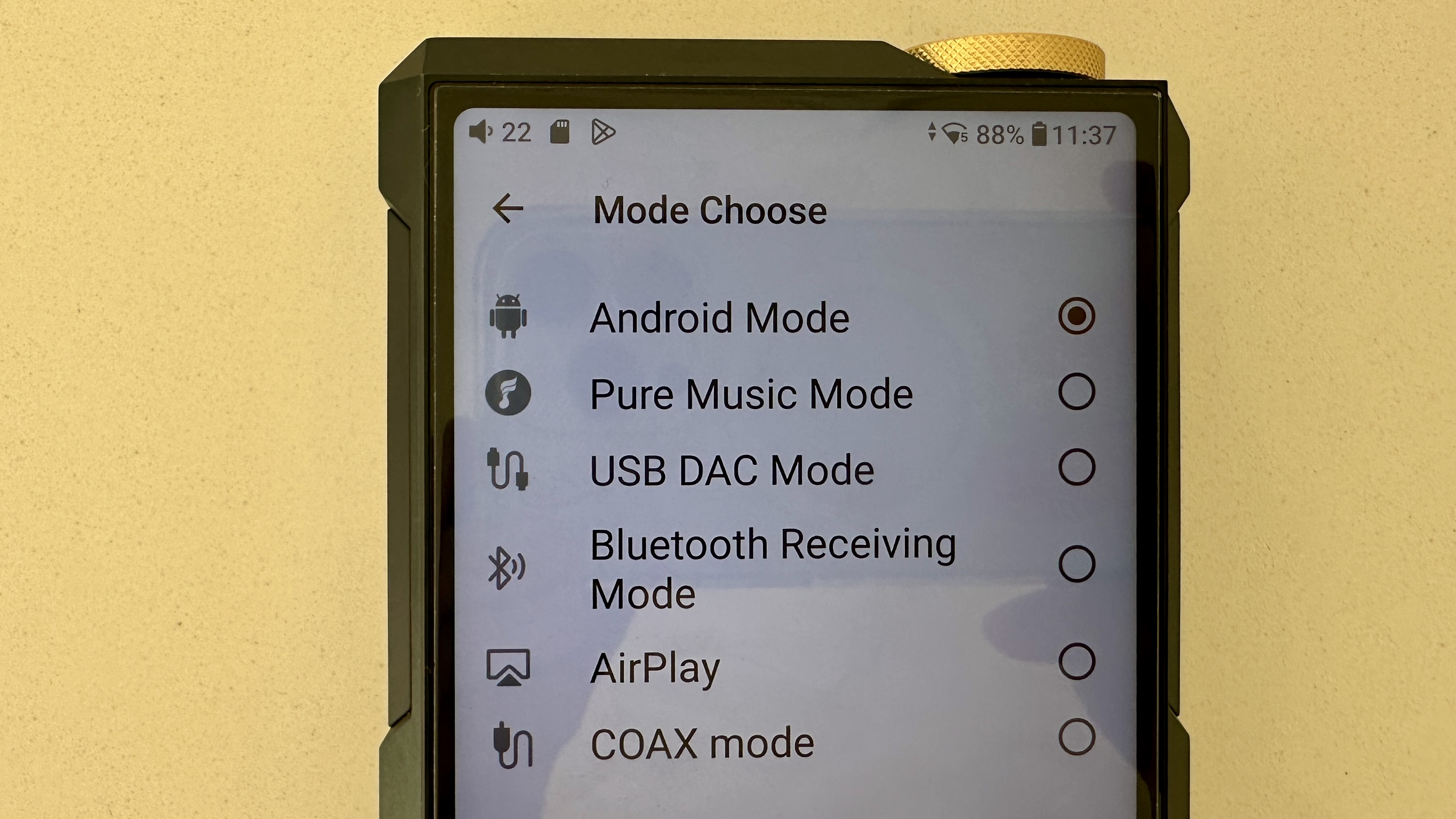 The FiiO M27 player with screen and dial showing, and content on the screen, on beige or yellow background