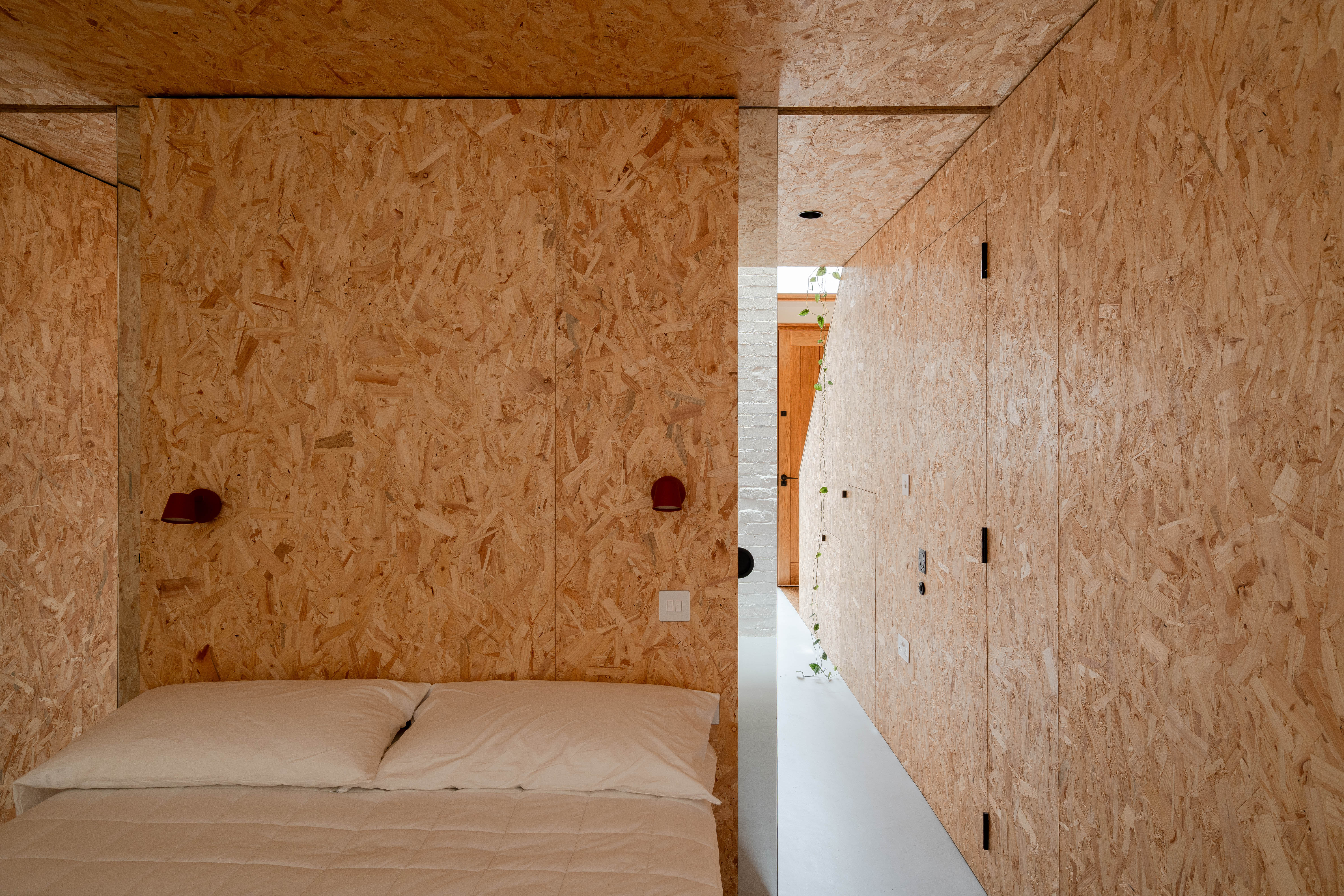 A bedroom with white bed and plasterboard walls down a long corridor