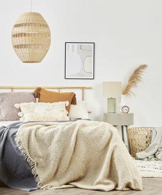 Relaxed bedroom in neutral palette, with tactile textures, pampas grass, and large natural materials ceiling pendant above bed.