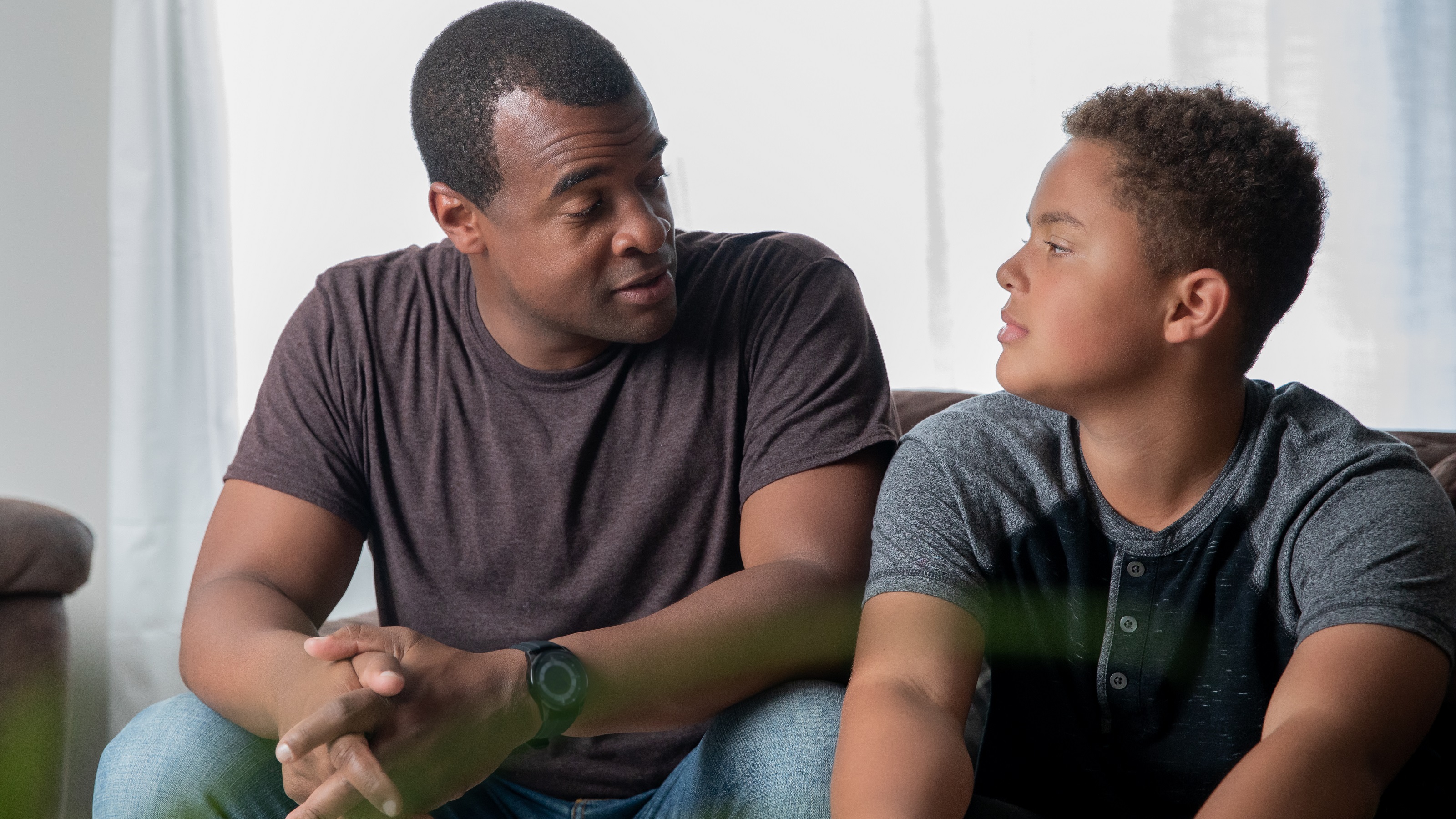 A father has a serious discussion with his son while they sit on the sofa.