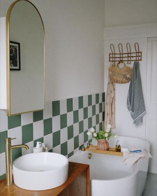 Bathroom with green and white tiles and gold metal accents and a deep white bath